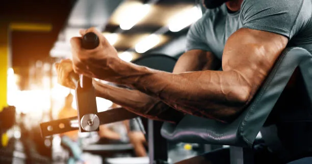 Close-up of muscular arms lifting weights with cardio equipment in the background