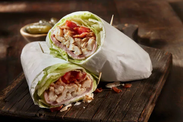Healthy fast food wrap filled with vegetables and lean protein on a wooden table